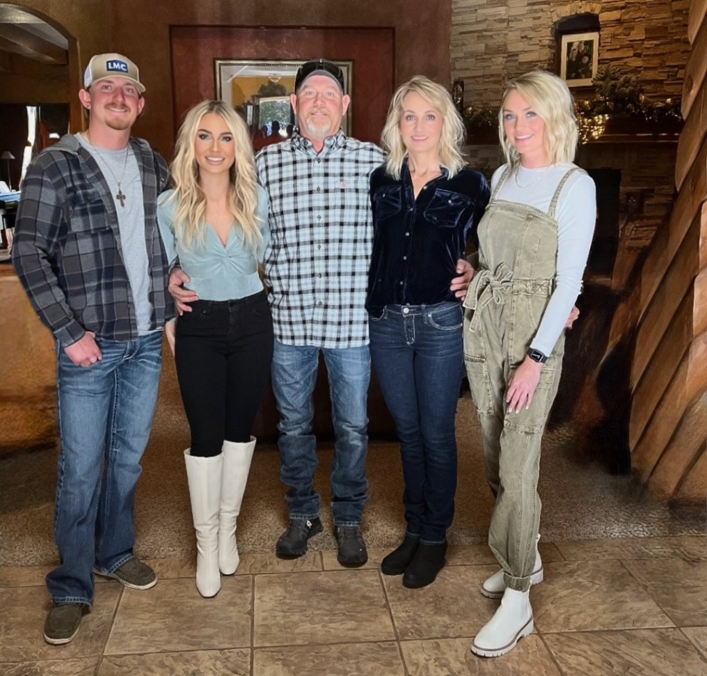 Five people pose for a group photo indoors, standing together in a rustic setting with stone and wood accents. The group includes three women and two men dressed in casual Western-style clothing.