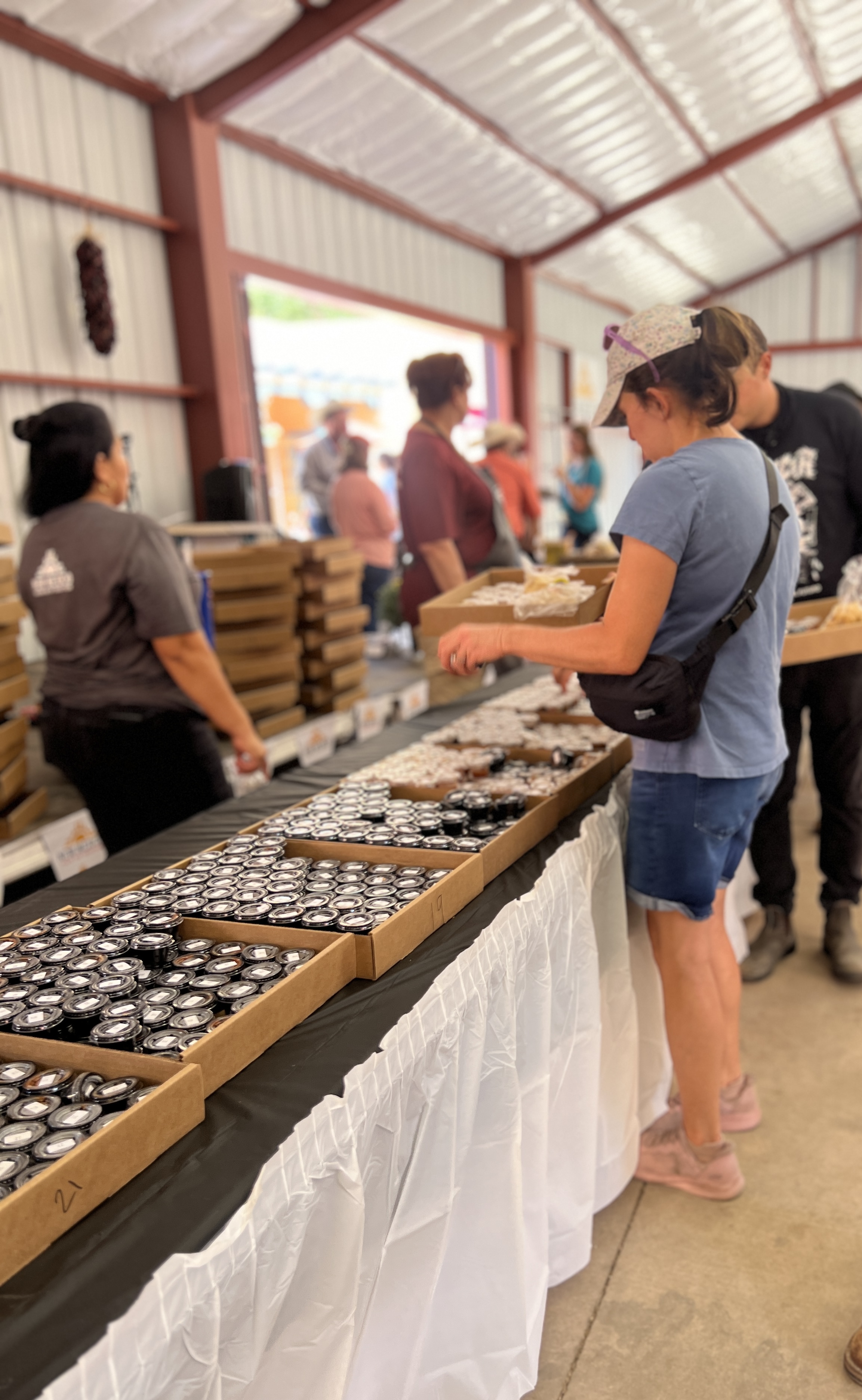 A woman selects small cups of salsa from cardboard trays, with event staff in the background.