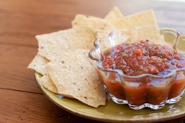 Close-up of salsa in a glass bowl and tortilla chips on a small yellow plate on a wooden table