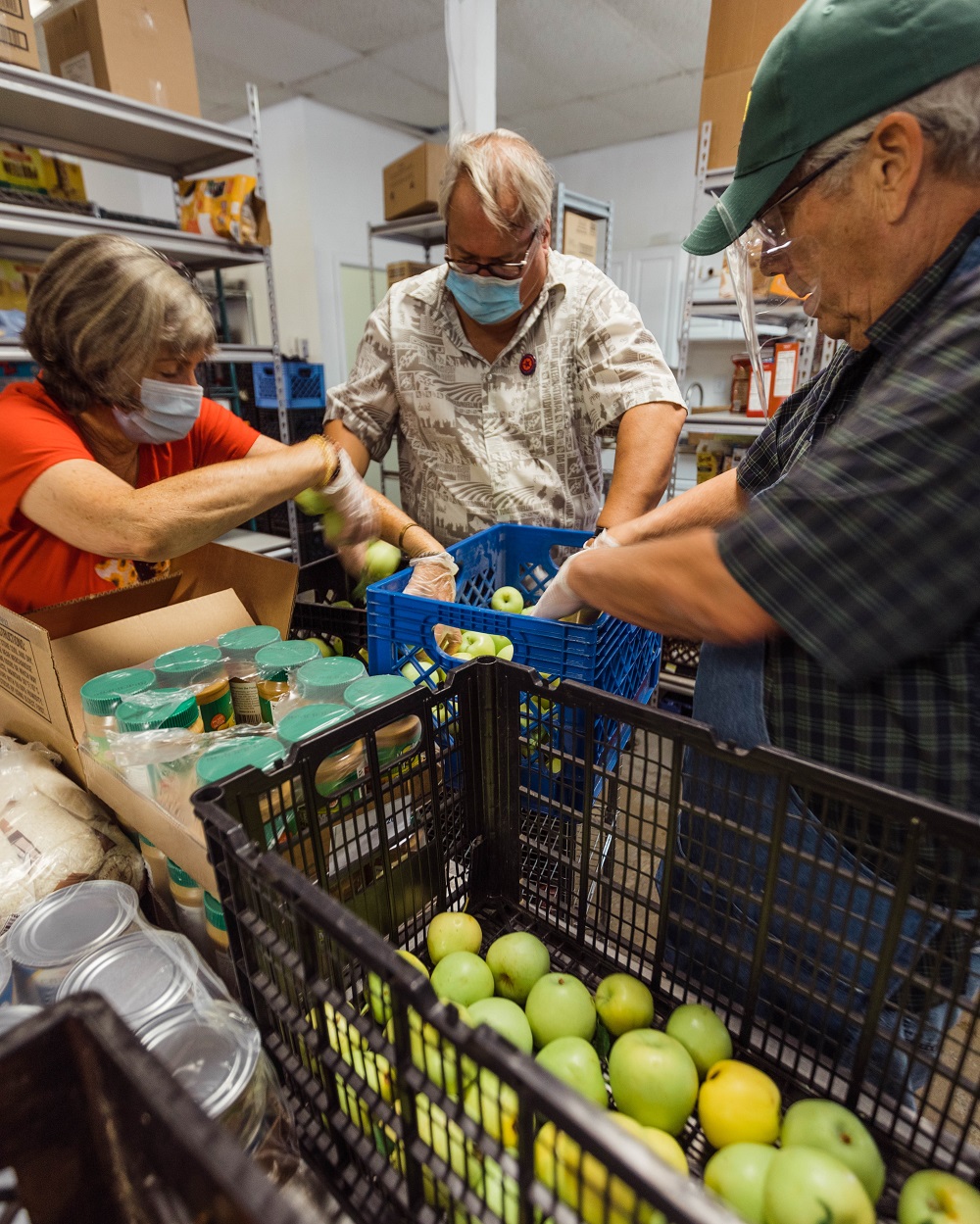 Two men and one women are sorting apples and peanut butter into bins and boxes.