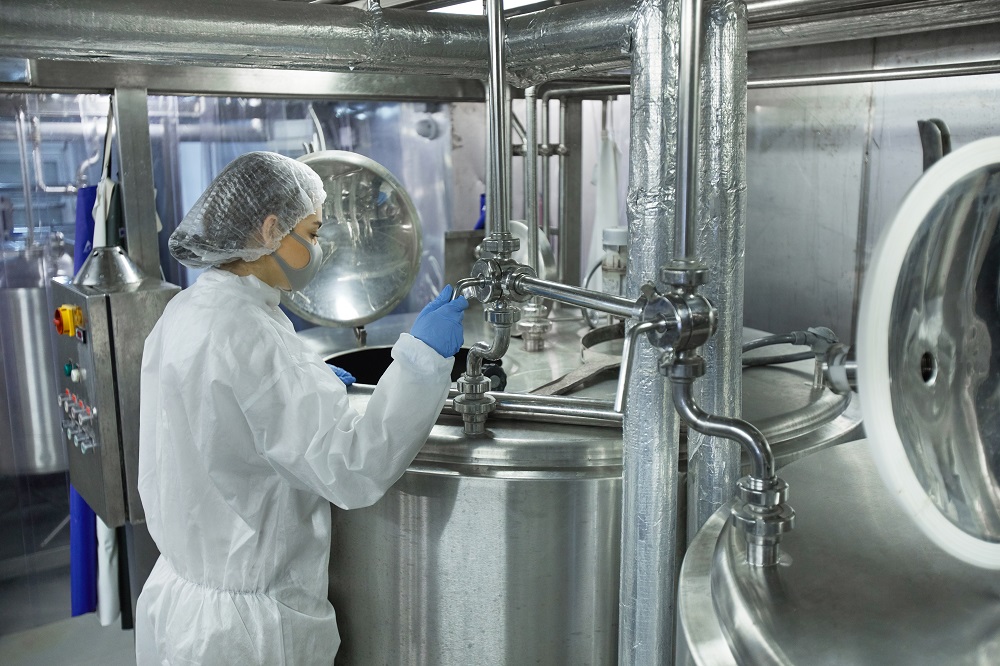 A woman inspecting a food processing facility dressed in personal protective equipment including a mask, gloves and a hair net. 