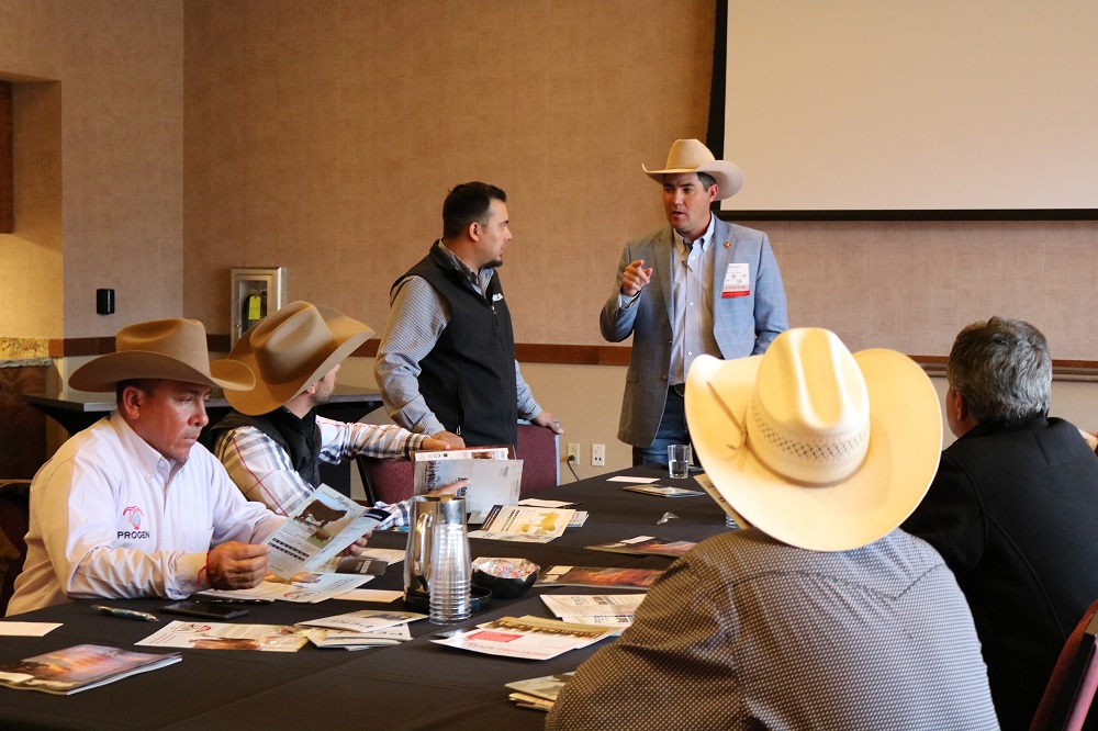 In a meeting room, gentlemen wearing cowboy hats are discussing the international cattle industry. 