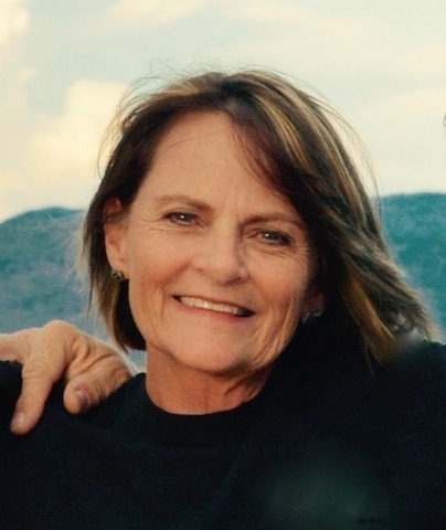 A woman in a black shirt with short brown hair with blonde highlights with mountains in the background. 