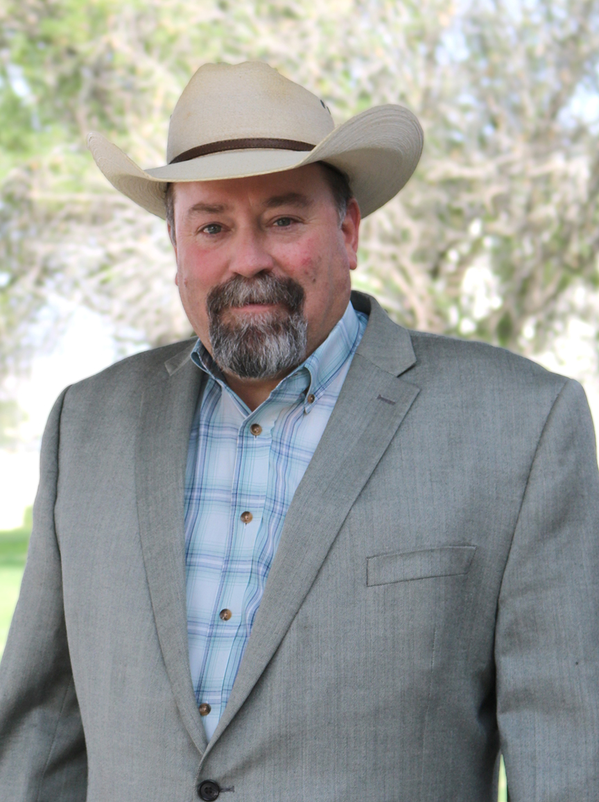 A man in a grey blazer, blue shirt and tan cowboy hat. 