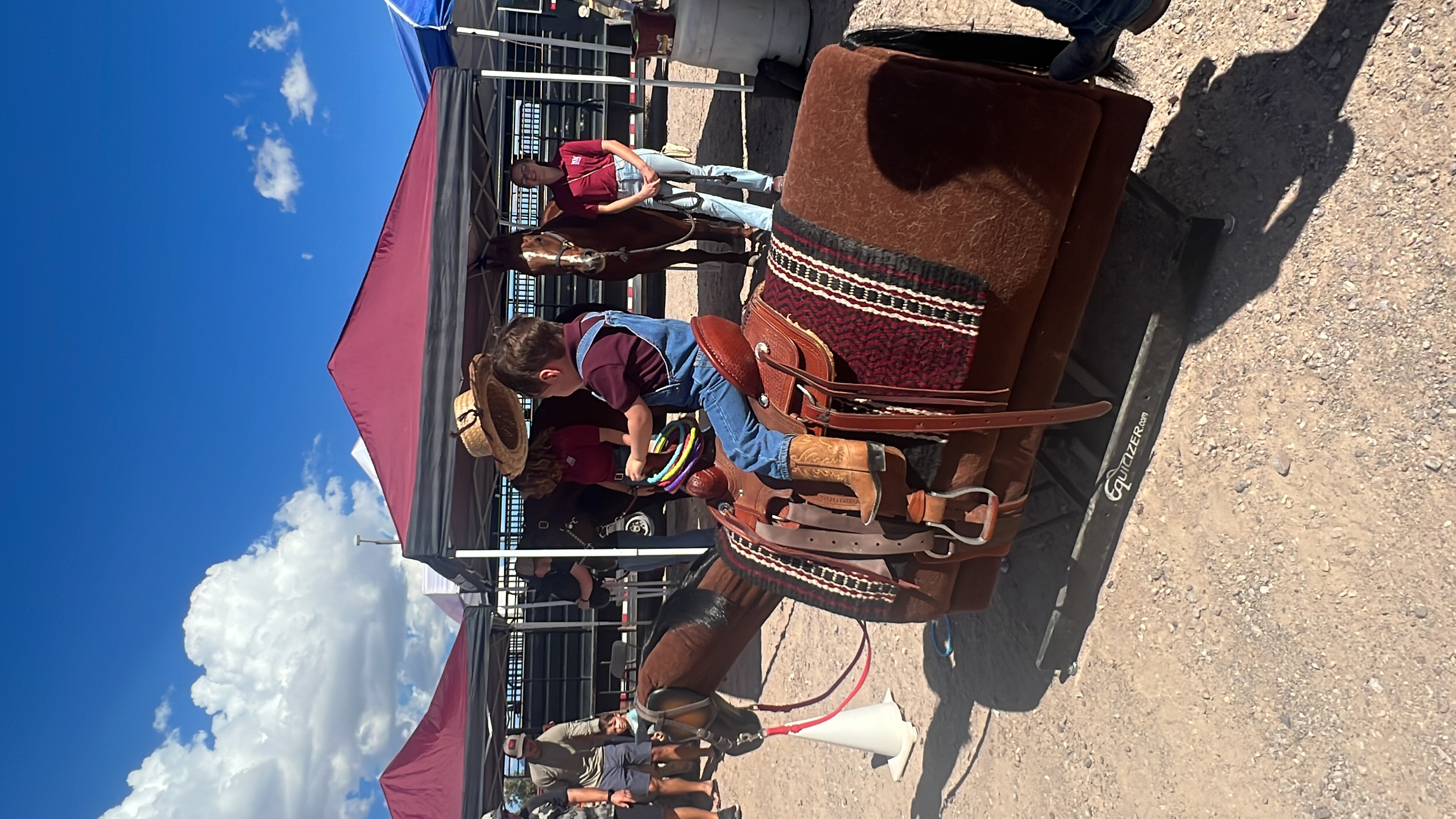 a young boy rides a rocking horse outside and tilts his hat