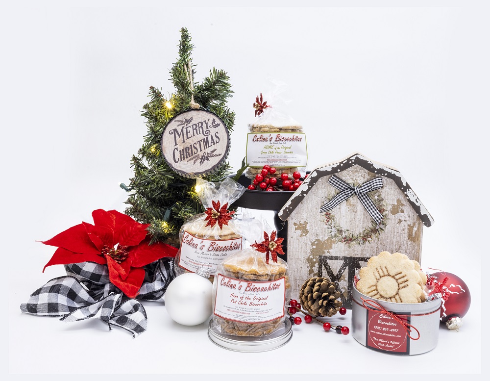 A Christmas scene filled with a tree, pinecones, ribbon and ornaments, sits different products from Celina’s Biscochitos. 