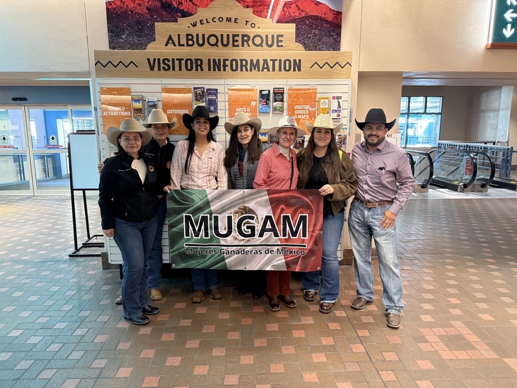 Members of Mujeres Ganaderas de México (MUGAM) pose with a banner at the Albuquerque International Sunport visitor information area during a trade mission visit to New Mexico.