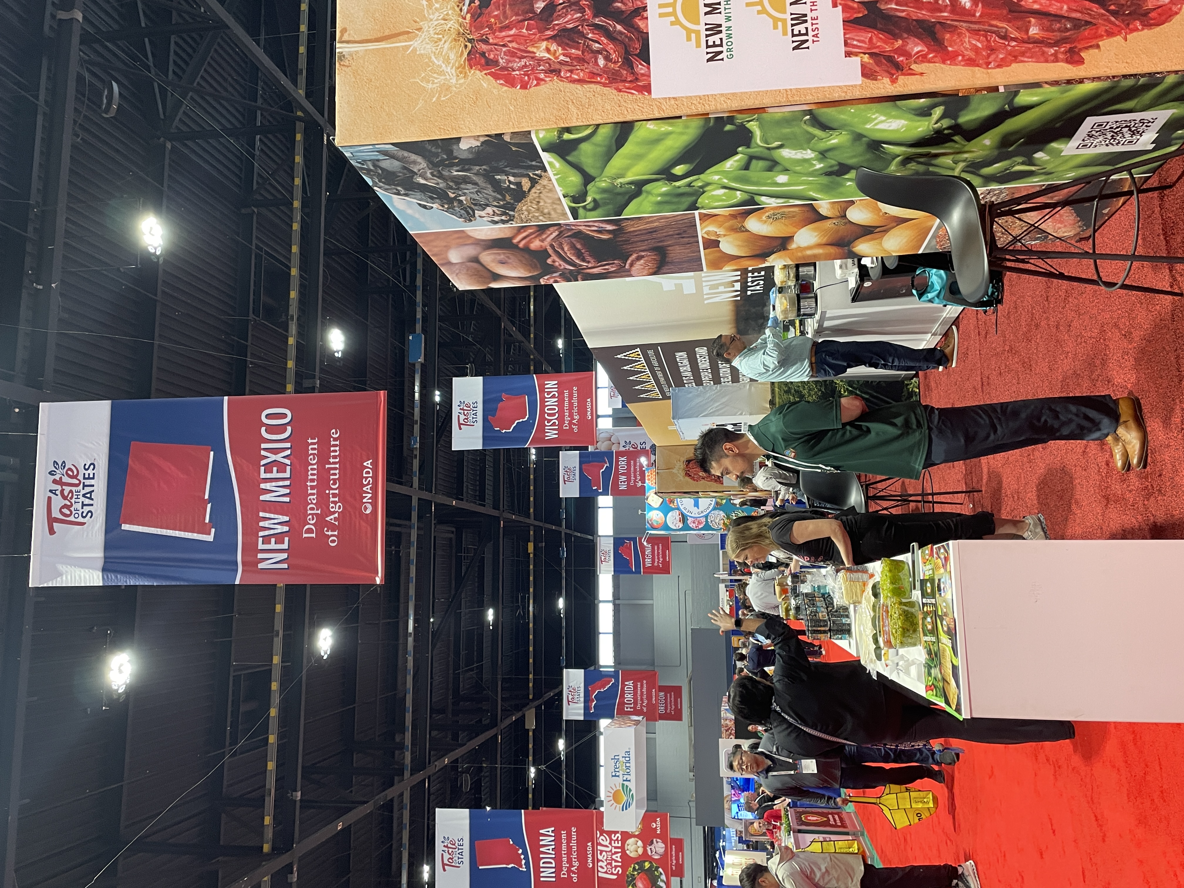 Attendees walk past the New Mexico "Taste the Tradition" booth at the Taste of the States exhibit, which features food samples and product displays.