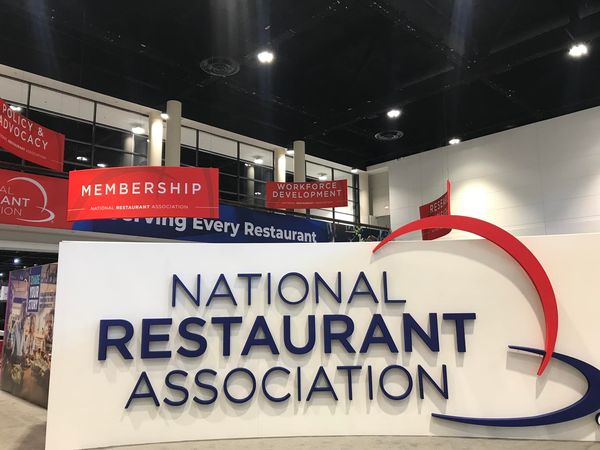 A white sign reads, “National Restaurant Association” in dark blue letters. Red and dark blue signs are in the background. 