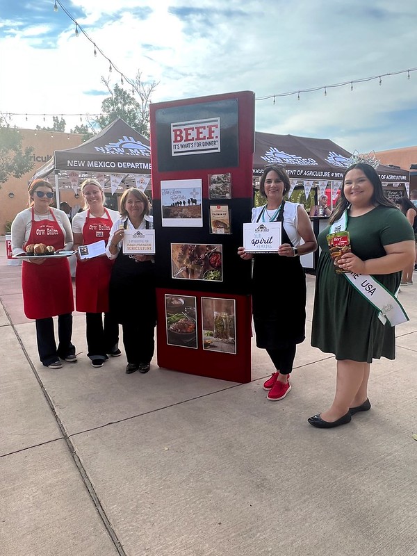 Cinco mujeres posan alrededor de un letrero que dice “New Mexico Beef Council” sosteniendo muestras y folletos.