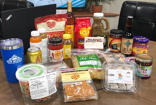 Numerous New Mexico products, including salsa, cookies, peanut brittle, beer, salsa, jam, honey and chips are arranged close together on a brown table.