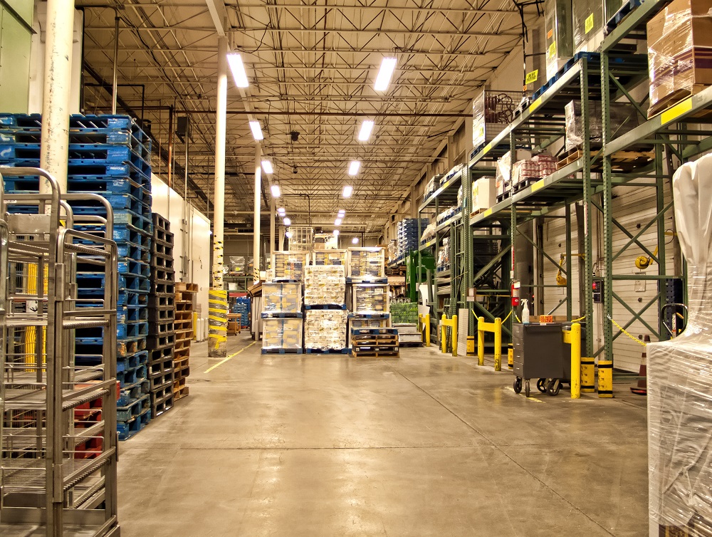 Inside of a brightly lit warehouse that shows green metal shelves and wooden pellets throughout.