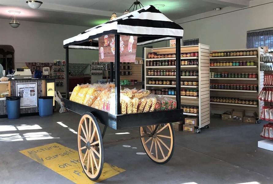 a black and white wagon with 2 wheels and a canopy carrying popcorn products from the country store.