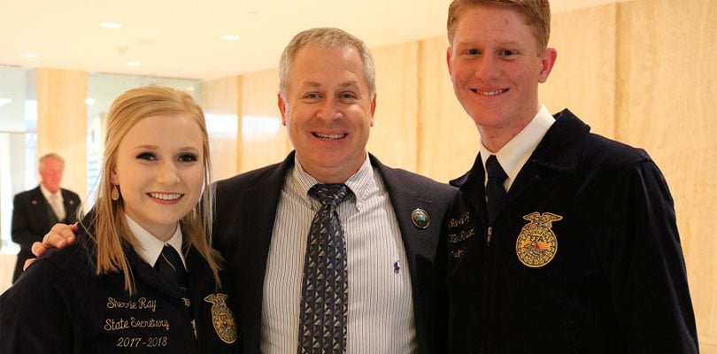 man standing between a young man and woman smiling. 